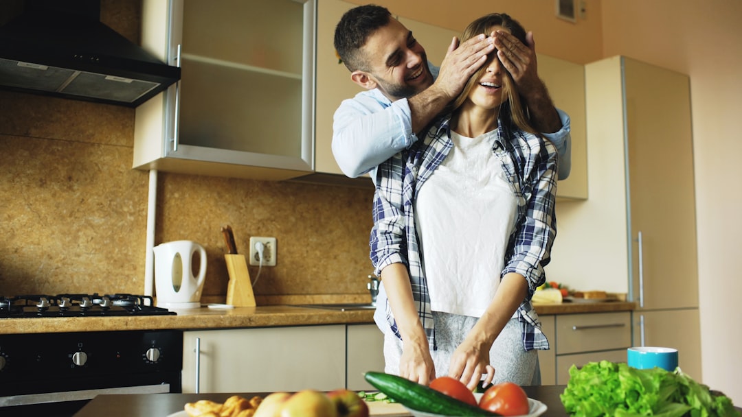 Man playfully covers woman's eyes in kitchen.