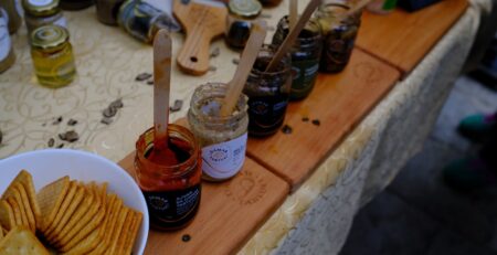 Jars of jams and spreads with crackers on a table.